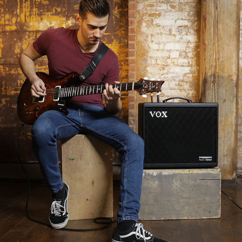 man playing electric guitar beside VOX amp