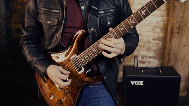 partial view of man playing electric guitar in front of VOX amp